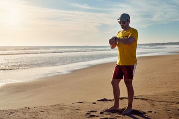 Barefoot hispanic mature man looking at his watch in his jogging routine on the beach