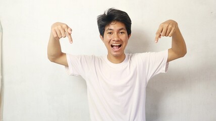 young asian man posing happily while pointing down on a white background