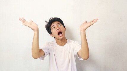 A young Asian man in a white shirt poses as if something has hit him from above and raises both...