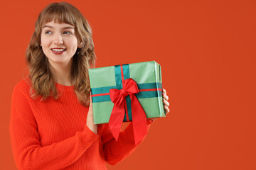 Beautiful young woman with gift box on orange background