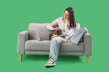 Obraz premium Young woman with cute British Shorthair cat and laptop on sofa against green background