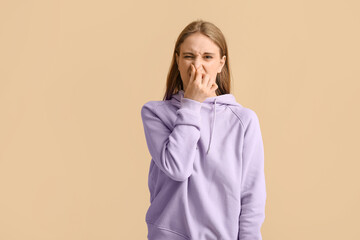Young woman  pinching nose because of disgusting smell on beige background