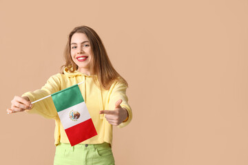 Beautiful young woman pointing at Mexican flag on brown background