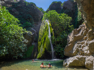 Small waterfall surrounded by plants and people cooling off in a calm basin (Richtis Gorge, Crete,...
