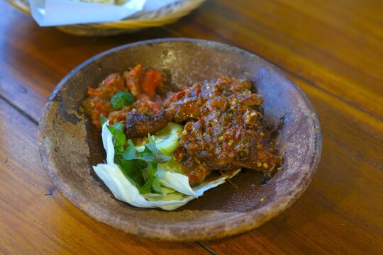 Ayam bakar, Indonesian roasted chicken served with chili sauce and raw vegetables on clay plate. Ayam bakar sdan ambal terasi