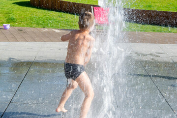 A boy playing with water in park fountain. Hot summer.