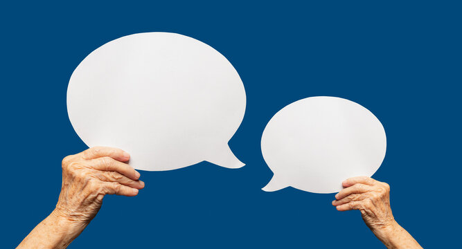 Close-up of a senior woman's hands holding a blank white speech bubble against a blue background.