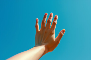 Closeup of woman's hand reaching out towards the sky, symbolizing hope and expression of dreams against clear blue background