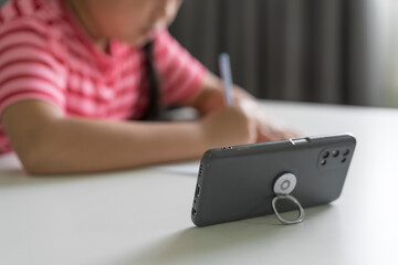closeup old smartphone with Asian child or kid girl student writing or drawing on paper to study online learning by mobile phone in classroom homeschool or young people learn from home and studying