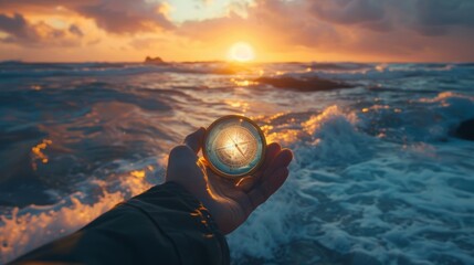 A hand holding a compass in front of a stormy sea at sunset - obrazy, fototapety, plakaty