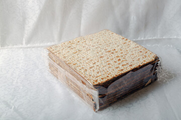 Box covered with matzah, an unleavened flatbread significant in Jewish Passover on a white tablecloth. The surface is perforated and browned, highlighting its baked texture. Matzo bread, unleavened
