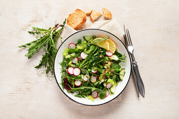Spring fresh salad with dandelion leaves, radish, cucumber on wooden background