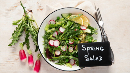 Spring fresh salad with dandelion leaves, radish, cucumber on wooden background