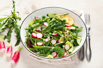 Spring fresh salad with dandelion leaves, radish, cucumber on wooden background