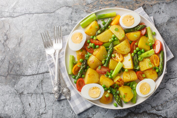 Fried new potatoes with asparagus, cherry tomatoes, boiled egg and green peas close-up in a plate on the table. Horizontal top view from above