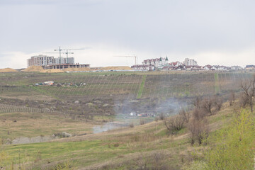View from a hill of a new residential complex and vineyards in a sinking town in spring, with smoke...
