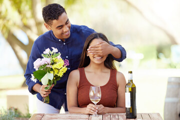 Man, woman and surprise with flowers, outdoor and cover eyes at restaurant with wine glass on date....
