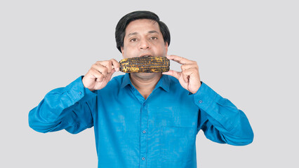 A young Indian male eating a corn cob with both hand, copy space on both sides