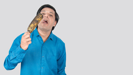 A Indian young male eating a corn cob with his facial expression, copy space on right side