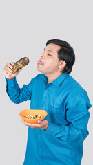 Portrait view of A young man looks desperate to eat a cob of corn in his hand and is showing his tongue with his crazy facial expression.
