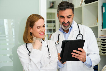 Two professional doctors talking about medical reports and using a tablet at office.
