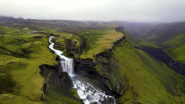 Beautiful Aerial Waterfall in Remote Landscape Eldgja Canyon. Epic Drone Around Green Mountain Canyon White Cascading Water Falls Into Blue Pool. Cloudy Foggy Mountains. 4K Color Corrected.