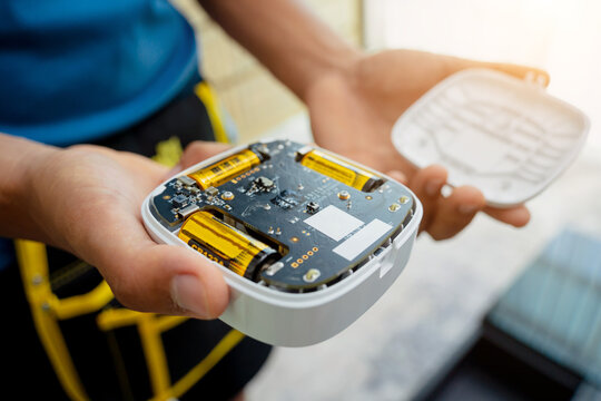 A technician installs a security alarm siren in a modern apartment.