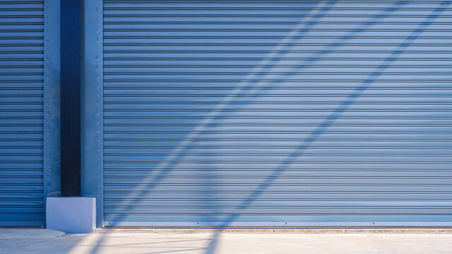 Automatic gray roller shutter entrance doors of large industrial warehouse building with light and shadow on concrete floor surface