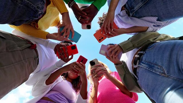 Young group of student women using smartphone together outside. Addicted millennial female friends using cell phone at city street. Low angle view.