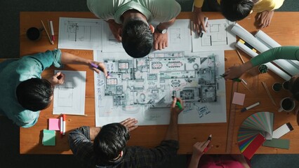 Top down view of civil engineer team writing at blueprint at meeting table with color palettes....