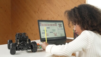 African girl writing car model structure while laptop display code. Smart student working by using...