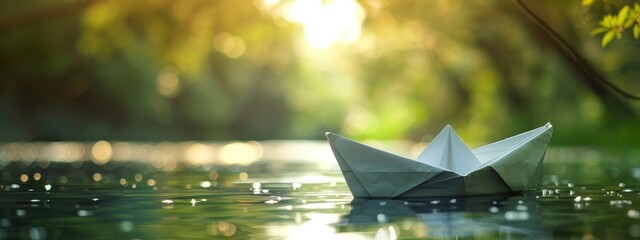 With sunshine peeking through the beautiful green trees in the backdrop, a paper boat floats on the water. - obrazy, fototapety, plakaty
