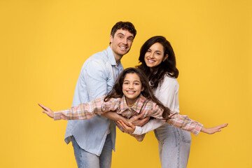 Family bonding concept. Joyful man and woman holding daughter on hands, girl pretending she is...