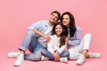 Full length shot of beautiful european family sitting on pink background, embracing and enjoying spending time with each other