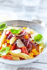Penne pasta with yellow and red pepper, hard cheese and fresh basil. Bright background. Close up.