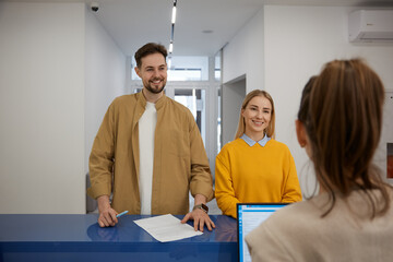 Happy man and woman couple signing document at modern clinic reception desk - obrazy, fototapety, plakaty