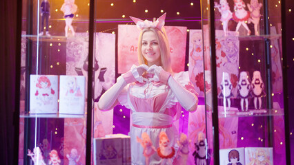 Cute pink cosplay maid girl give a heart sign at anime art stand