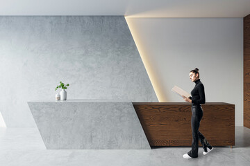 A woman stands by a modern reception desk in an office lobby with a gray background, showcasing a...