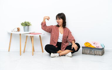 Young mixed race woman folding clothes sitting on the floor isolated on white background doing...