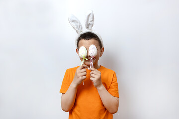 A boy with bunny ears and holding decorated Easter eggs.