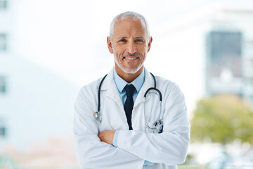 Doctor, happy and portrait of mature man in a hospital at a cardiology clinic with arms crossed....