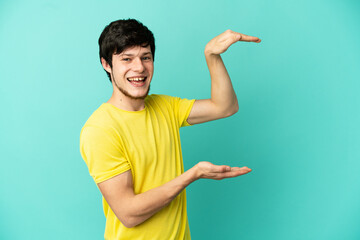 Young Russian man isolated on blue background holding copyspace to insert an ad