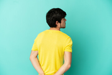 Young Russian man isolated on blue background in back position and looking back