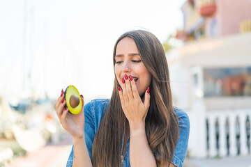 Young woman holding an avocado at outdoors with surprise and shocked facial expression