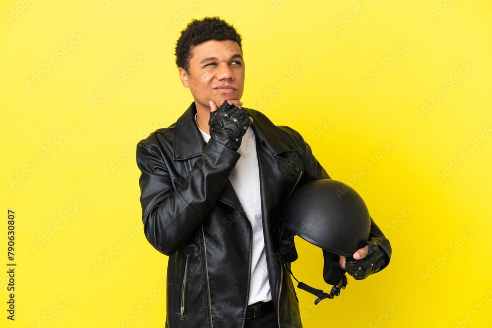 Wall mural young african american man with a motorcycle helmet isolated on yellow background and looking up