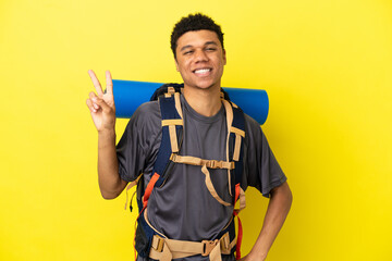 Young mountaineer African American man with a big backpack isolated on yellow background smiling...