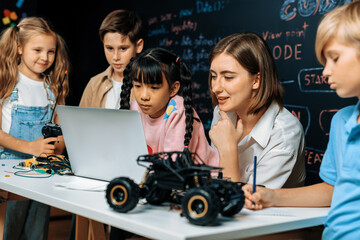 Skilled kids learning to program remote car. Schoolgirl in pink cloth use laptop for coding. Other...