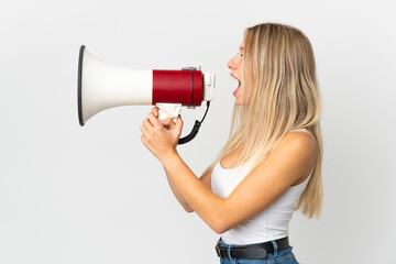 Young blonde woman isolated on white background shouting through a megaphone to announce something...