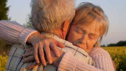 Elderly grey haired caucasian woman saying goodbye with love hugs husband tightly. Happy couple...