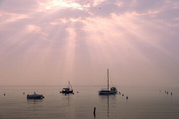 The evening sun rays pierce the clouds, casting a soft, ethereal glow over the boats and waterfowl...